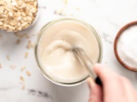 A jar of oat milk being stirred with a metal straw, as seen from above.