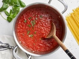 Overhead view of finished marinara sauce in the pot surrounded by pasta and herbs.