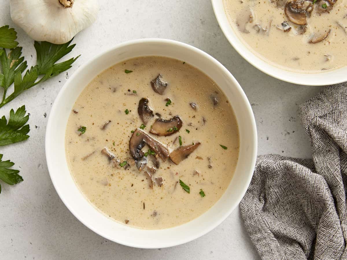 Overhead view of two bowls of mushroom soup garnished with parsley. 