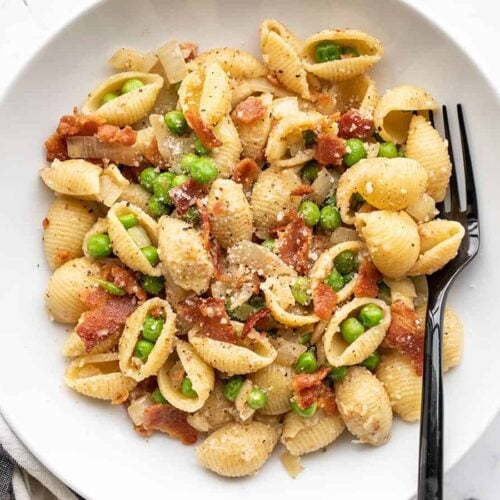 Close up overhead view of a bowl of pasta with bacon and peas.