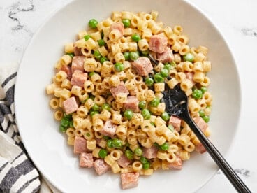 Overhead view of a bowl full of pasta with peas and ham and a fork.