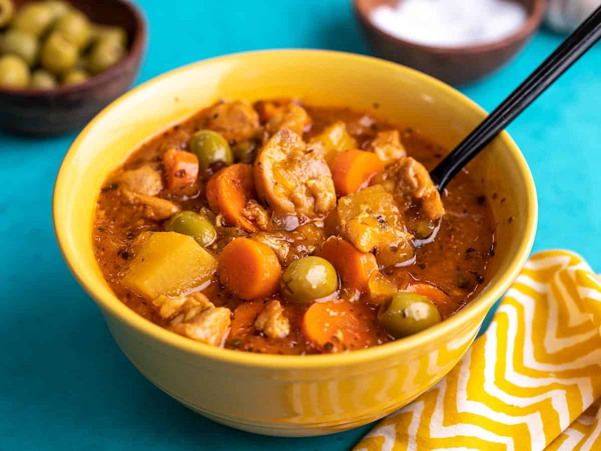 Side shot of Guisado de Pollo in a yellow bowl with a spoon in it.