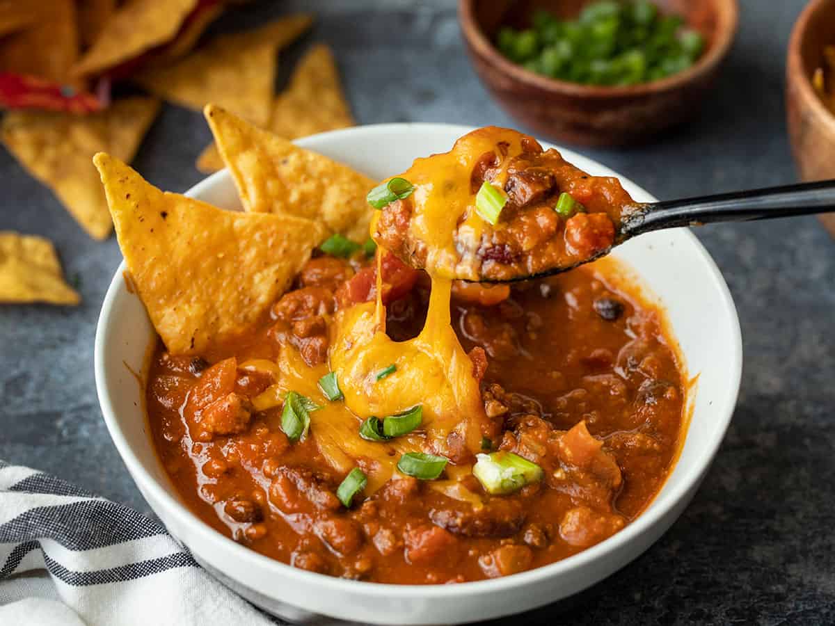 A spoon lifting a bite of pumpkin chili with melted cheese stretching from the bowl