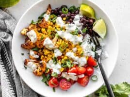 Close up overhead view of a roasted cauliflower taco bowl topped with cilantro lime ranch and a black fork in the middle