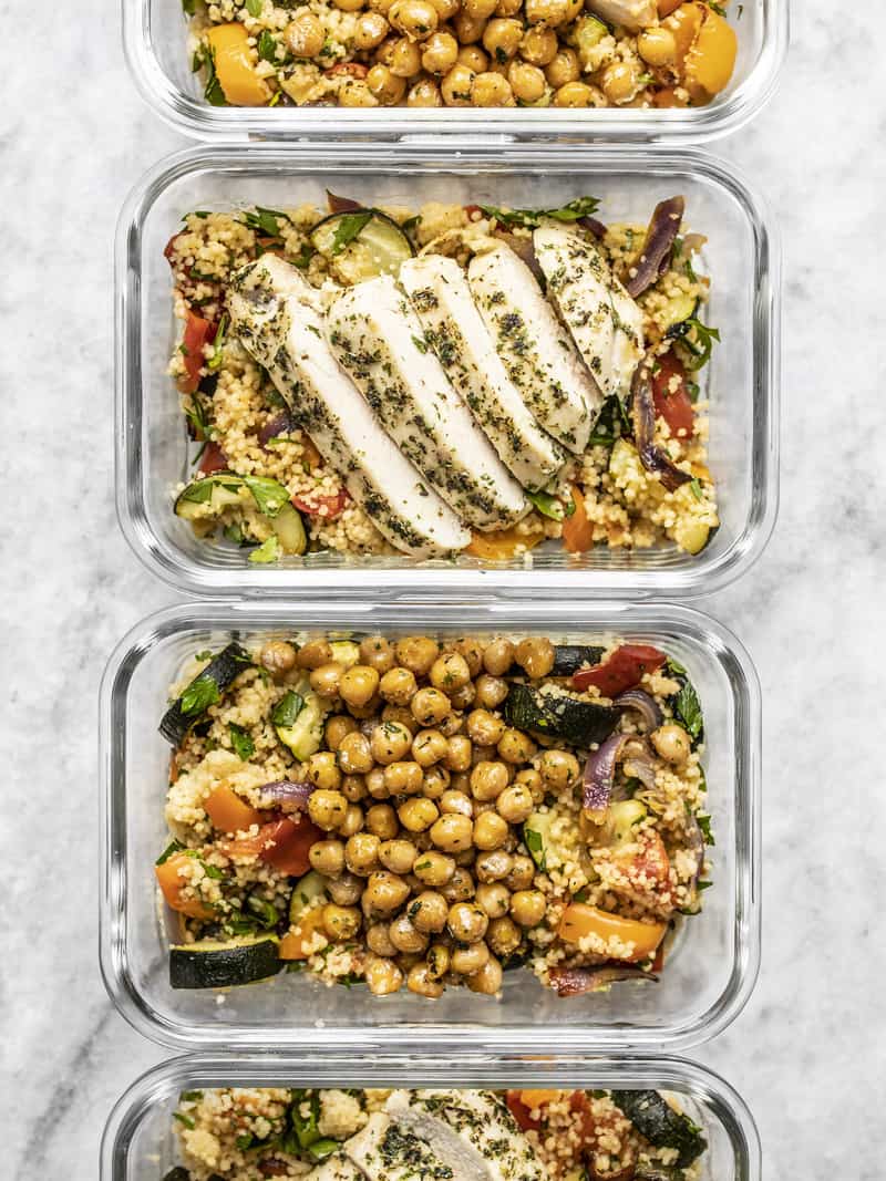 Four glass meal prep containers lined up with Roasted Vegetable Couscous and Garlic Herb Baked Chicken or Garlic Herb Chickpeas