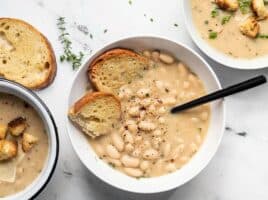 Three bowls of rosemary garlic white bean soup with different toppings (pesto, croutons, Parmesan).