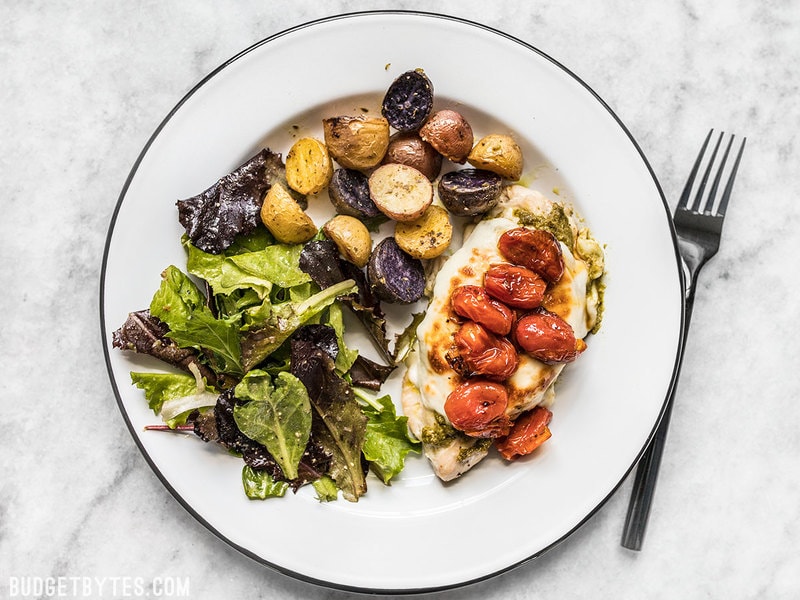 A plate full of Sheet Pan Pesto Chicken Dinner, complete with roasted potatoes and tomatoes, and a simple side salad. 