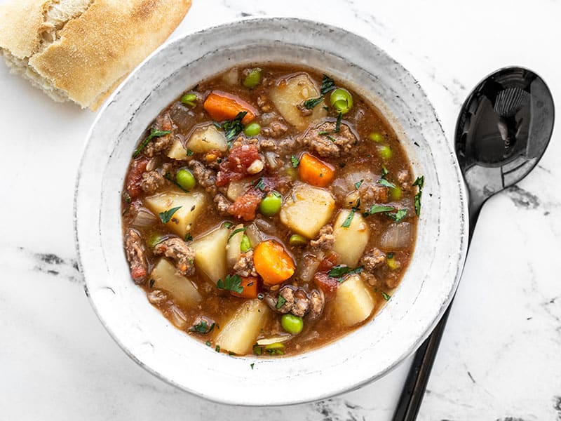 Overhead view of a bowl full of slow cooker hamburger stew with bread and a spoon on the side