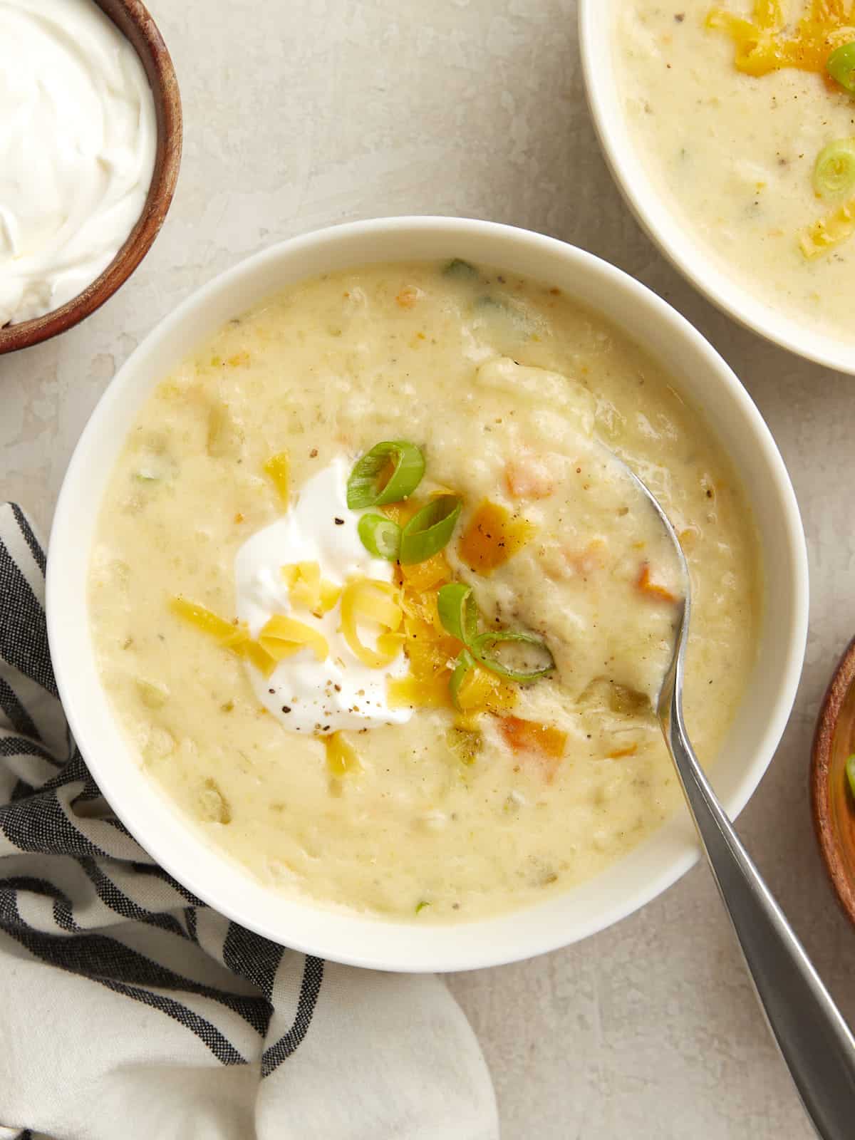 Overhead photo of slow cooker potato soup in a white bowl with sour cream, green onions, and shredded cheese on top.