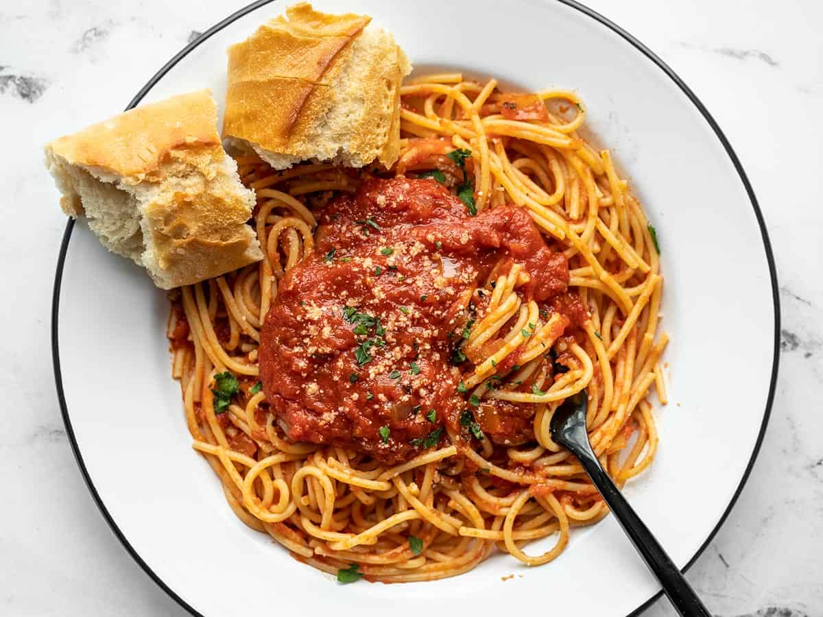 A plate of pasta covered in sauce with bread on the side