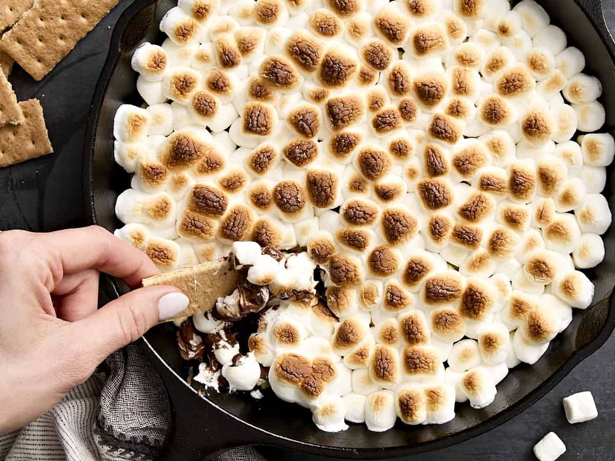 A hand dipping a graham cracker into s'mores dip