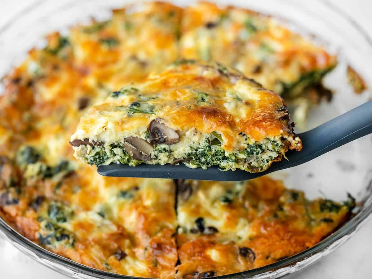 A slice of crustless quiche being held in front of the pie dish on a spatula