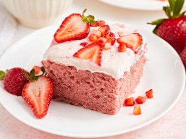 Close up view of strawberry sheet cake on a white plate with fresh strawberries on top.