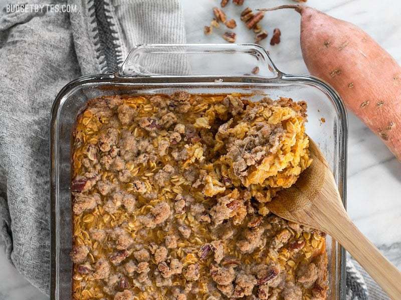 Sweet Potato Casserole Baked Oatmeal in the glass casserole dish being scooped out by a wooden spoon, viewed from above.