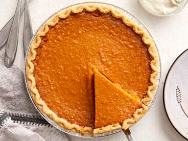 Overhead view of a whole sweet potato pie with one slice cut and being lifted out of the pie pan.