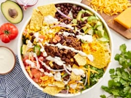 overhead view of taco salad with creamy white dressing and corn chips in a white bowl.