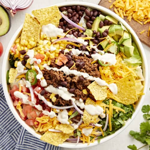 overhead view of taco salad with creamy white dressing and corn chips in a white bowl.