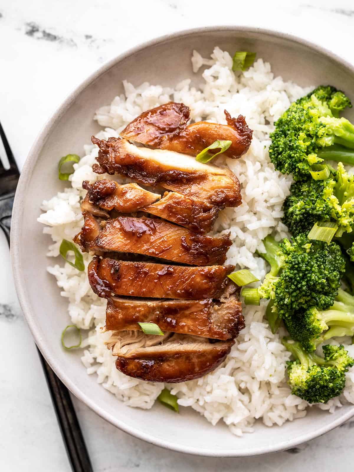 sliced teriyaki chicken on a bed of rice next to broccoli.