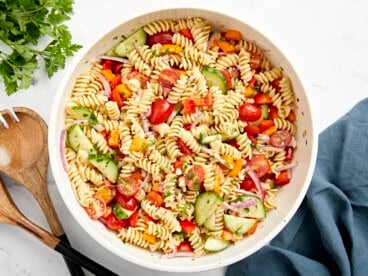 Overhead view of pasta salad in a large white serving bowl with wood serving utensils on the side.