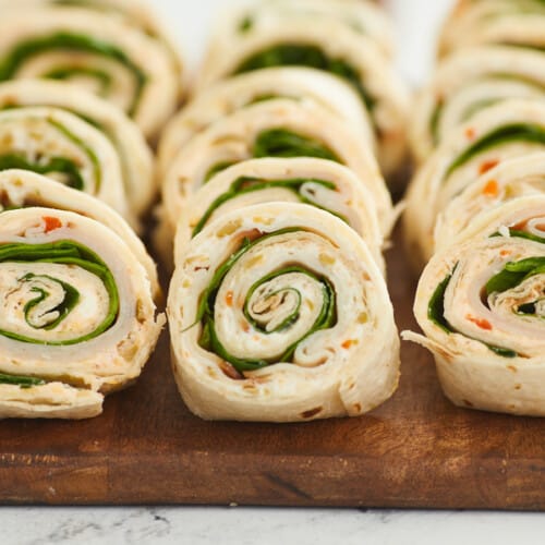 A close up of three rows of turkey pinwheels on a wooden cutting board.