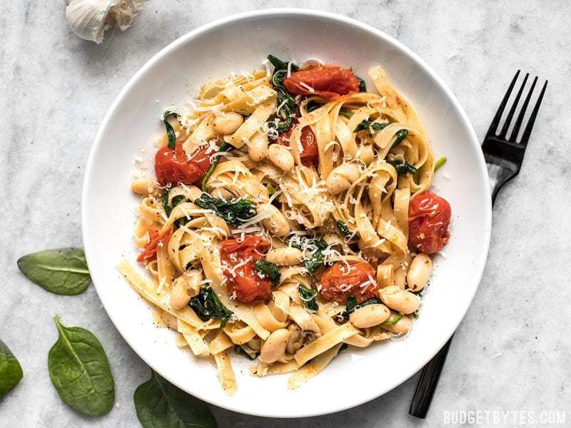 Tuscan White Bean Pasta in a bowl, topped with Parmesan, a black fork on the side