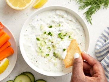 Overhead view of tzatziki sauce with a pita chip being dipped in the sauce.