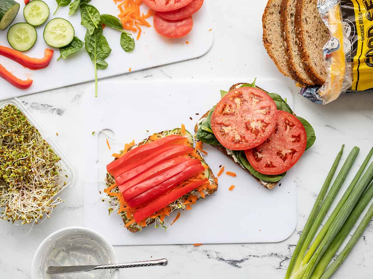 A veggie sandwich being built, ingredients all around.