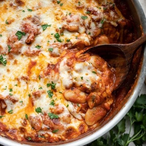 Close up view of a spoon scooping some white beans with mushrooms and marinara, garlic bread on the side.